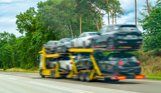 A yellow car carrier truck transports multiple cars on a highway near Flint, MI, surrounded by trees and greenery, with motion blur indicating speed—perfectly capturing Car Transport Flint,MI in action.