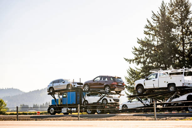Bright blue industrial car hauler classic carrier big rig semi truck tractor transporting cars and crossovers on hydraulic modular semi trailer driving on the divided highway road in California
